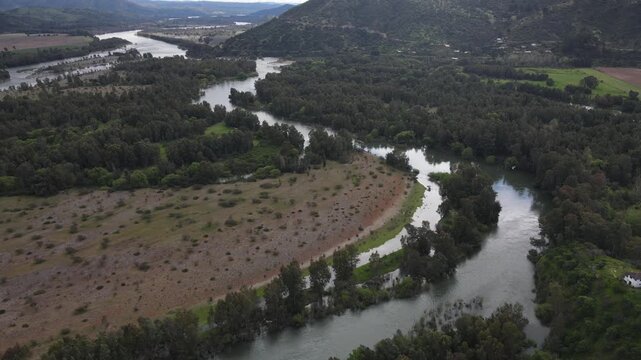 Aerial glide over the remote Rio Claro and Rio Maule confluence in Maule Region Chile, with reflective river bends, forest, fields and low hills.