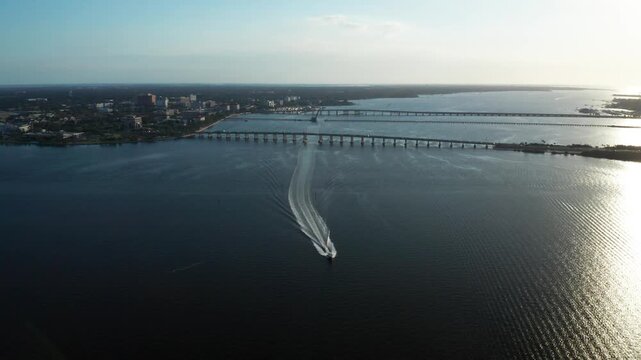 Motorboat speeds toward two long bridges on the Manatee River as fading evening light reflects on calm water.