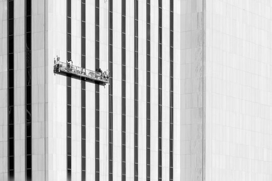 Window washers cleaning the glass facade of a skyscraper on a suspended platform represent industrial labor and commercial development in Lower Manhattan, New York City, USA.