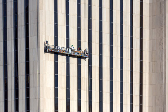 Window cleaners on a suspended scaffold maintain a high-rise office facade, showcasing a professional urban lifestyle of industrial labor in Lower Manhattan, New York City.