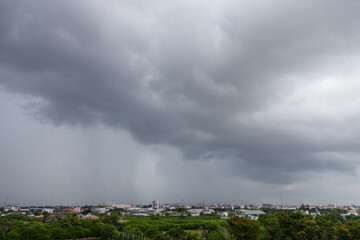 Fototapeta premium A high angle view overlooking a green, tree filled area and a city skyline, with heavy rain falling from dark, dramatic storm clouds.