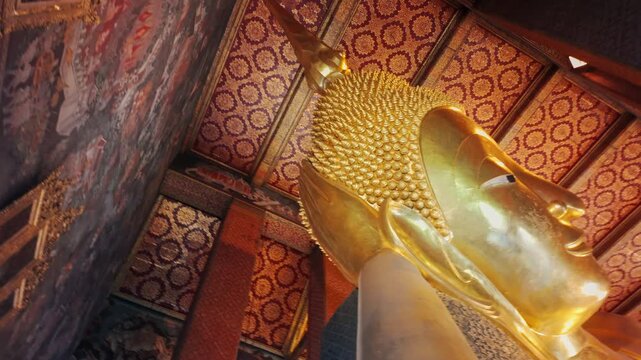 BANGKOK, THAILAND, 5 October 2025 &ndash; A low-angle shot captures the serene face and golden body of a Reclining Buddha statue inside a temple, showcasing intricate ceiling details.