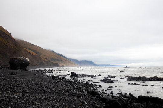 View of the rugged Lost Coast featuring a black sand beach, large boulders, and steep hills under an overcast sky in Humboldt County, California, United States.