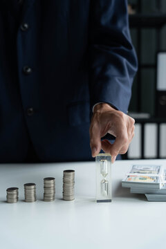 Businessman with coin stacking and hourglass on table, investment and time concept