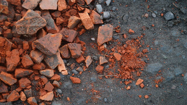Broken Red Clay Bricks and Shards Scattered on Dark Volcanic Sand Ground