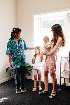 Doctor in patterned scrubs gently touching child&rsquo;s head beside mother and baby