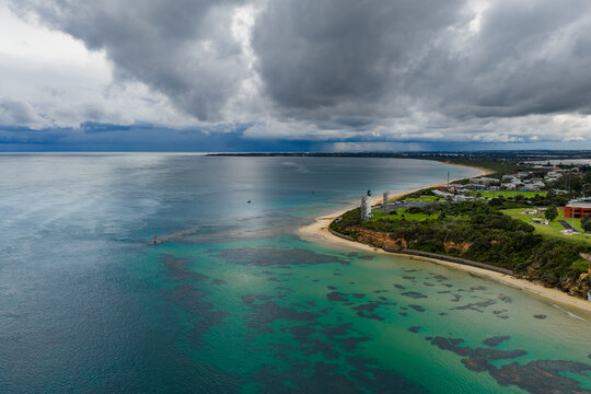Aerial wide angled view of a lighthouse on a coastal point off a calm bay with dramatic storm clouds