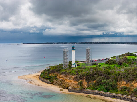 Aerial view of dramatic cloud bank and rain advancing over a coastal lighthouse above a beach