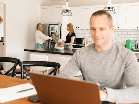 Teenage daughter helping mum with groceries in the kitchen while dad works on computer