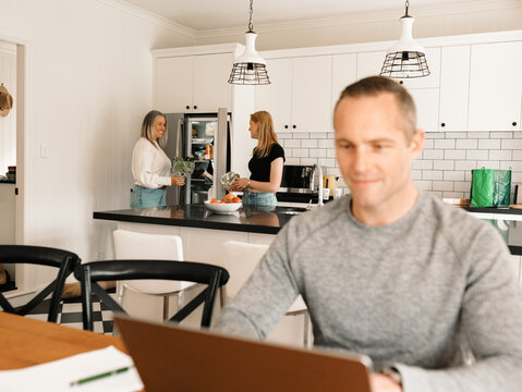Teenage daughter helping mum with groceries in the kitchen while dad works on computer