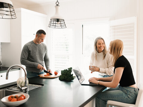 Family preparing food and using laptop in kitchen