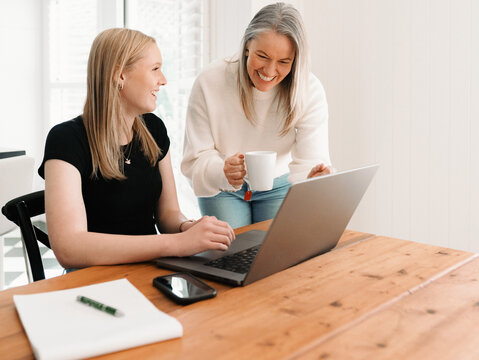 Mum leaning over teenage daughter working on her laptop on the wooden table
