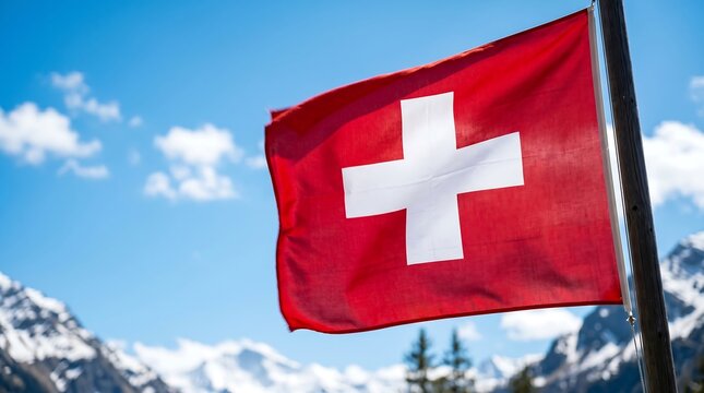 Swiss flag waving on wooden pole against snowy Alpine mountain peaks and clear blue sky background