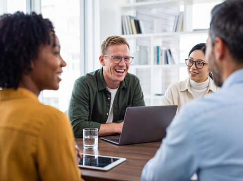 Diverse professional colleagues engaging in lively conversation and laughter around a table during an office discussion.