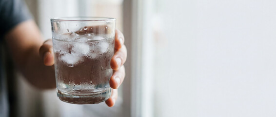 Fototapeta na wymiar Person's hand carrying a glass of water filled with ice cubes, showing condensation for a cool drink