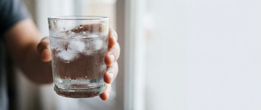 Person's hand carrying a glass of water filled with ice cubes, showing condensation for a cool drink