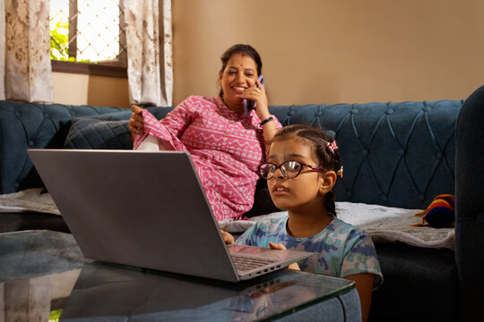 Daughter using a laptop while mother talks on the phone