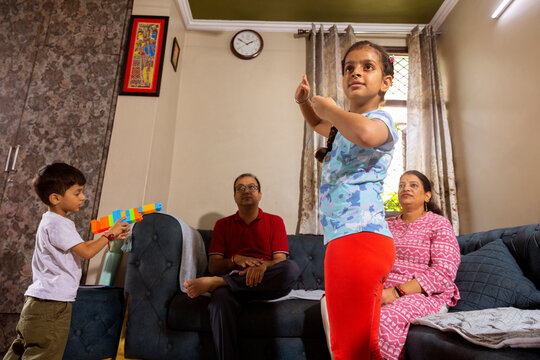 daughter dancing at home with her parent watching and brother playing in background