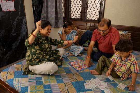 mother and daughter victory dance in snakes and ladder games against father and son is playing cards