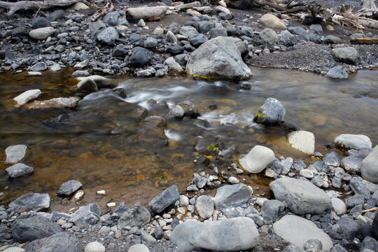 View of a clear stream flowing over smooth grey stones and pebbles along the rugged shoreline of the Lost Coast in Humboldt County, California, United States.