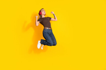 Obraz premium Happy young woman jumping with red headphones against bright yellow background expressing joy and energetic music listening