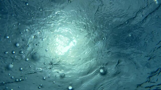 Swimmer enjoys refreshing dive in crystal-clear tropical pool. Aquatic leisure and relaxation concept. Sunlight creates beautiful patterns as bubbles rise, enhancing tranquil atmosphere