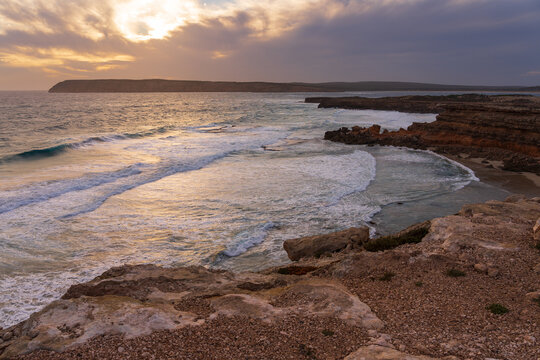 High view looking down over waves breaking on a rugged eroded coastline at sunset