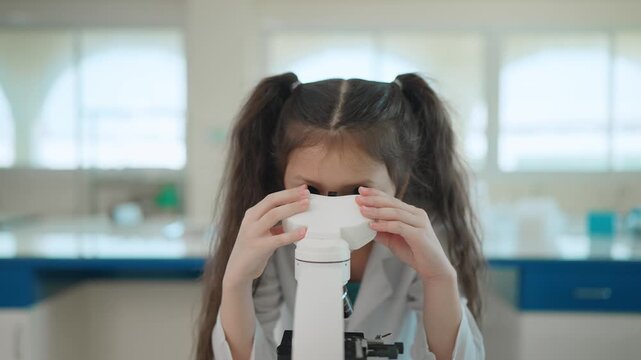 Curious Young Scientist: A young girl with pigtails, wearing a lab coat, peers intently through a microscope in a brightly lit laboratory, showcasing a budding interest in science and discovery.