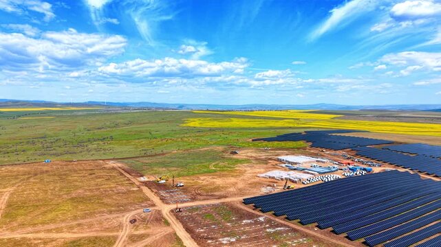 Solar power plant construction site with materials and machinery. Aerial view of a solar farm under construction showing material pallets, drilling machinery, and new panels.