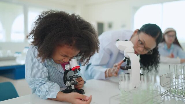 Curiosity in the Lab: A young girl with curly hair intently observes through a microscope in a bright, modern laboratory, a mentor beside her guiding the scientific exploration.