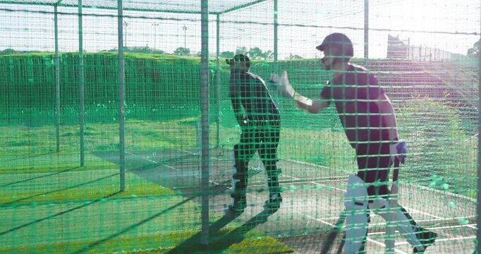 Diverse male players measuring run-up, bowling, defending with bat for training in cage on turf