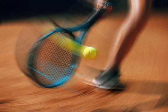 Tennis racket striking ball with dynamic motion blur on court. Concept of tennis action poster, speed and motion blur, athletic competition, dynamic sports advertising.