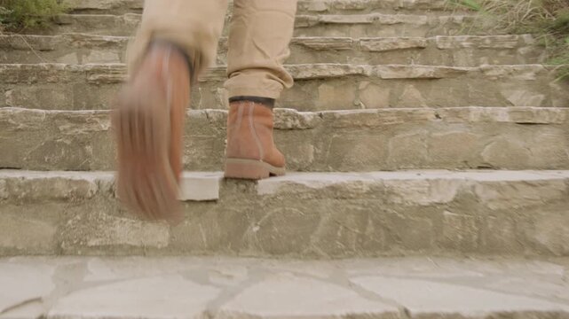 Feet in boots climb up stone steps of stairs outdoors close-up.