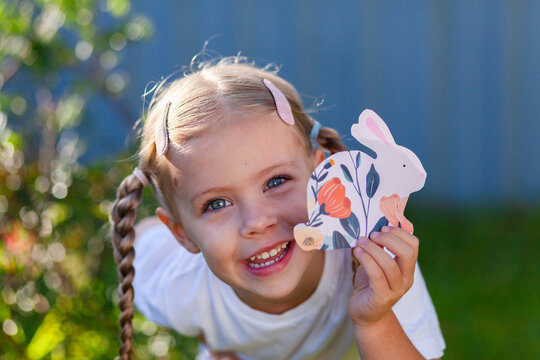 Child holding paper rabbit cutout in backyard at easter