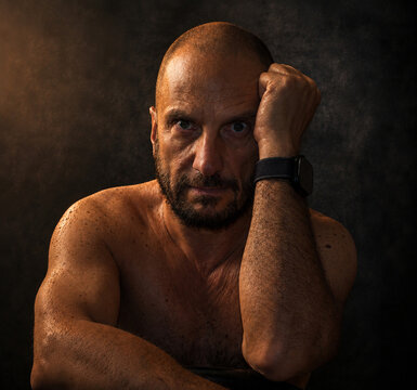 Dramatic portrait of a bald mature man with muscular physique against dark background