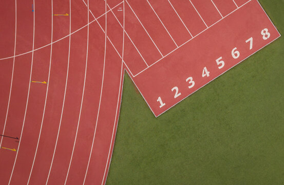 Top-down nadir aerial view of a red athletics track showing curved oval lanes meeting straight sprint lanes with numbered starting positions 1-8 and green grass infield