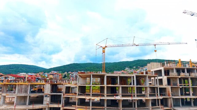 Multi story concrete building structure construction site with crane. Framework of a large building under construction with a yellow tower crane against a backdrop of hills and town.