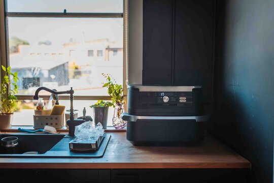 Kitchen counter with air fryer beside sink, natural light from window