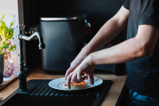 Teenager placing cooked pizza pie on plate after cooking in the air fryer