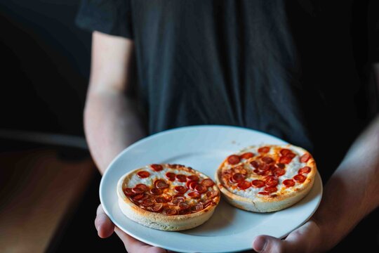 Hungry teenager holding a plate with two cooked mini pepperoni pizzas