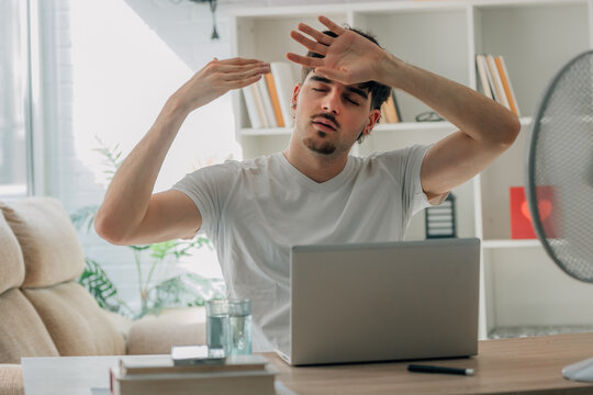 young man at home studying and working on a laptop during a summer heat wave