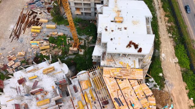 Direct overhead aerial view of complex building construction site. Top view of reinforced concrete building slabs with yellow wooden formwork panels and construction materials.