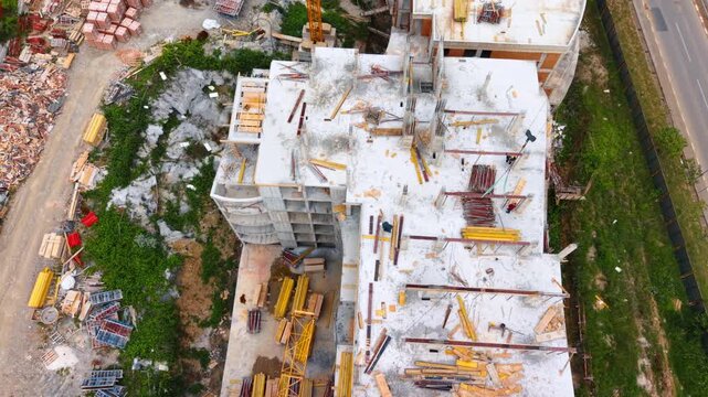 Vertical drone shot of concrete building framework and materials. High angle look down at concrete floor slabs, yellow formwork boards, scattered materials and a tower crane.