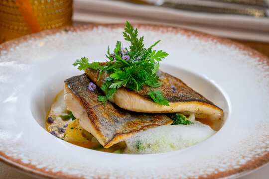 Close up of pan seared fish fillet with crispy skin. Detailed close up of fried white fish fillets garnished with fresh green parsley and small purple flowers.