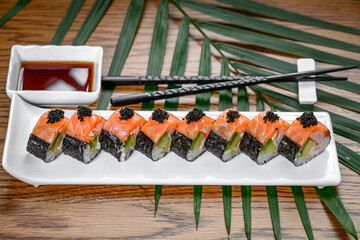 Salmon maki sushi rolls with black roe on plate. Salmon sushi rolls with black caviar, avocado filling, served on white ceramic plate with chopsticks and palm leaves. © Анна Терелюк