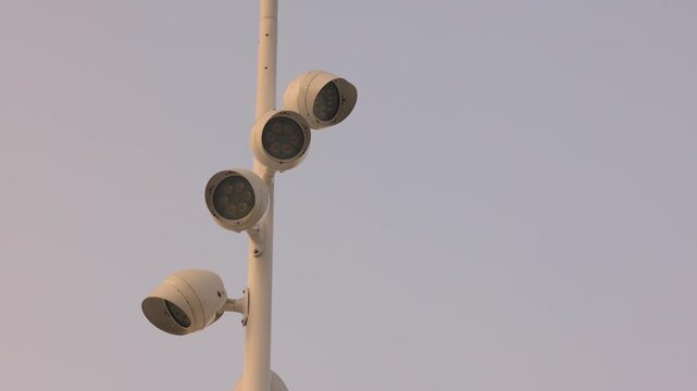 Outdoor surveillance cameras on poles with metal shields against blue sky