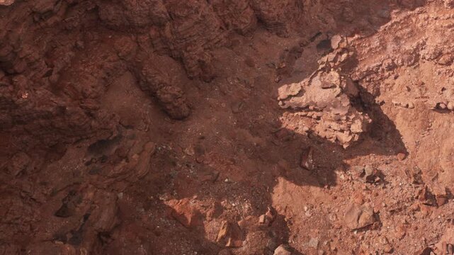 The scene shows a rocky surface characterized by various formations and textures. The ground appears dry with little vegetation. The colors are mostly red and brown, indicating an arid environment.