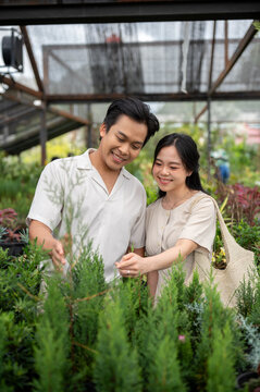 Smiling asian man and woman couple choosing plant enjoy shopping in greenhouse nursery garden center