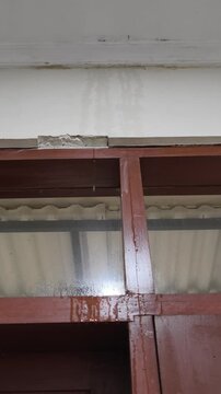 Water dripping continuously from a cracked white ceiling onto a brown wooden window frame due to a severe roof leak damage.