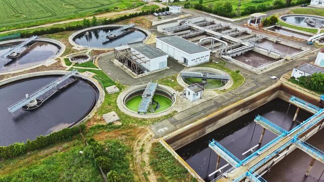 Aerial wastewater treatment plant circular basins showing clarifier tanks and aeration systems, sludge channels, blue mechanical scrapers, concrete service